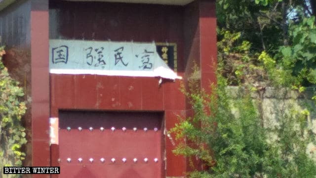 Caratteri cinesi di significato religioso coperti dai caratteri che significano «La nazione è forte, la gente prospera» sulla cancellata di una famiglia nella contea di Xin'an