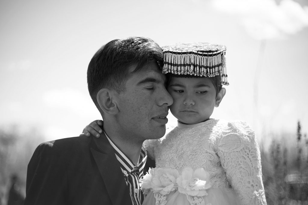Un uomo porta affettuosamente sua figlia, vestita per una festa di famiglia. 