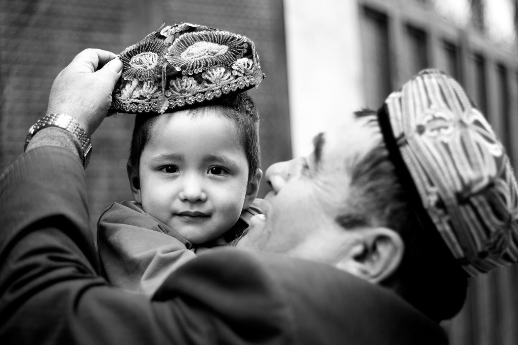 Un uomo mette una doppa ricamata (il tradizionale cappello) sul capo del figlio