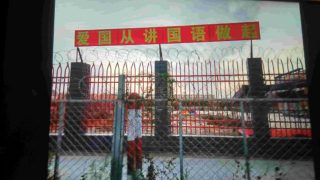 Muro perimetrale dell'asilo munito di filo spinato. Il cartello dice: «L’amore per il tuo Paese inizia parlando in cinese mandarino»