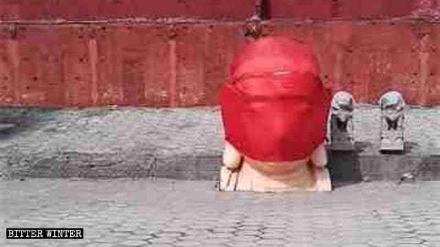 La testa di una statua del Buddha demolita avvolta in un panno rosso