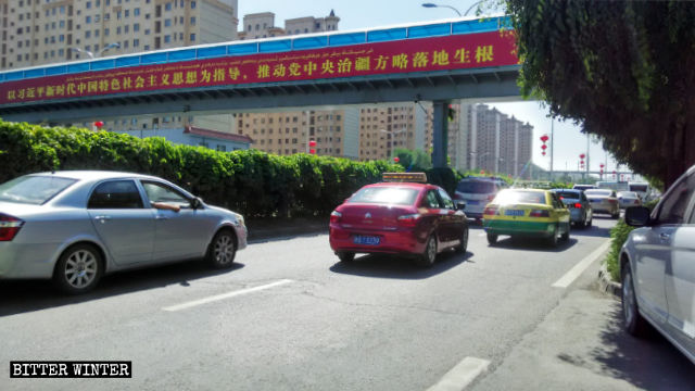 Un cartellone con slogan di propaganda a Uruqi: «Promuovi la piena applicazione della strategia della Commissione centrale del Partito per governare lo Xinjiang», secondo il pensiero di Xi Jinping