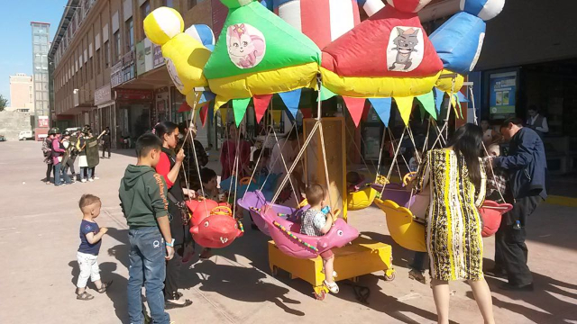 Immagini contrastanti dallo Xinjiang: bambini che giocano sulla giostra e sullo sfondo la «milizia territoriale» del mercato di Hotan che si sta addestrando