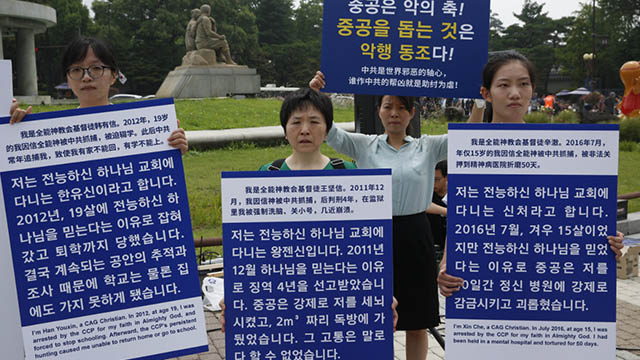 I fedeli della CDO reggono cartelli che raccontano brevi storie della persecuzione patita, denunciando il PCC come il centro di un “asse del male” internazionale