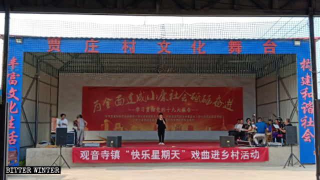 Uno spettacolo è in corso nel Teatro culturale del villaggio di Jiazhuang e sul palco è appeso uno striscione con scritto «Domenica felice»