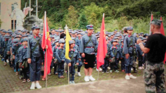 Gli studenti indossano l’uniforme dell’Esercito Popolare di Liberazione e portano zaini con stampati il ritratto del presidente Mao e lo slogan «Servire il popolo»