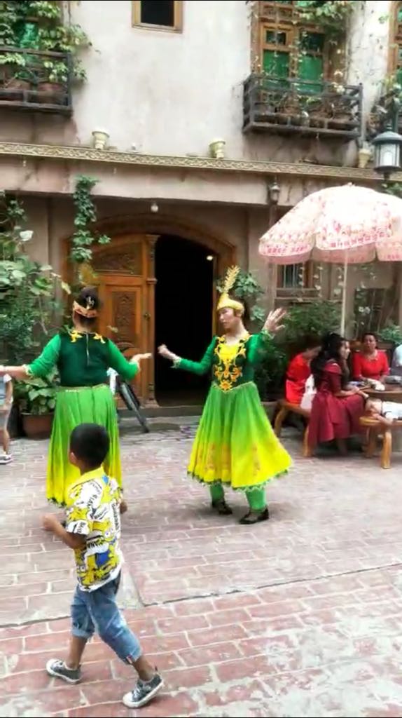 Ragazze uigure dall'espressione triste costrette a danzare per i turisti han a Kashgar