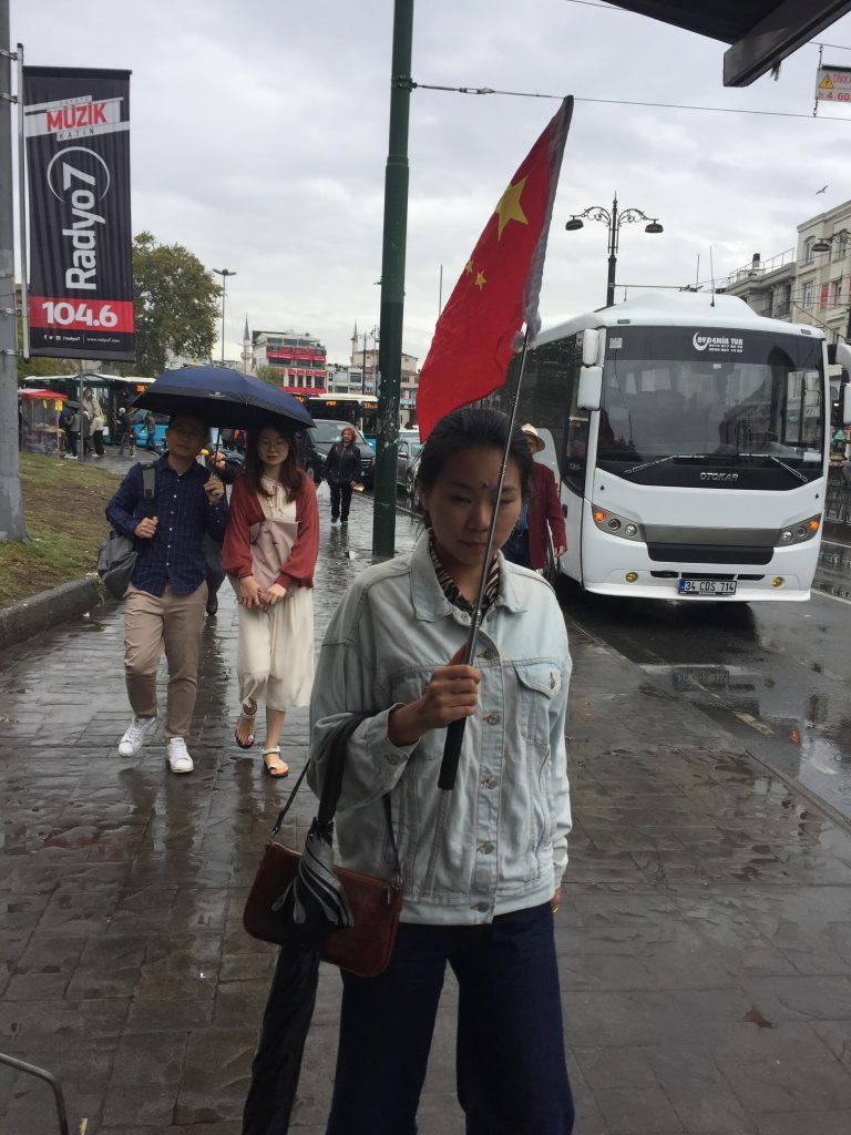 La bandiera rossa cinese sventola alta sopra le vie di Istanbul, mentre una guida turistica accompagna i visitatori attraverso gli antichi bazar