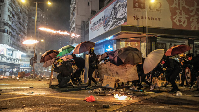 I manifestanti di Hong Kong si difendono dai lanci di lacrimogeni della polizia